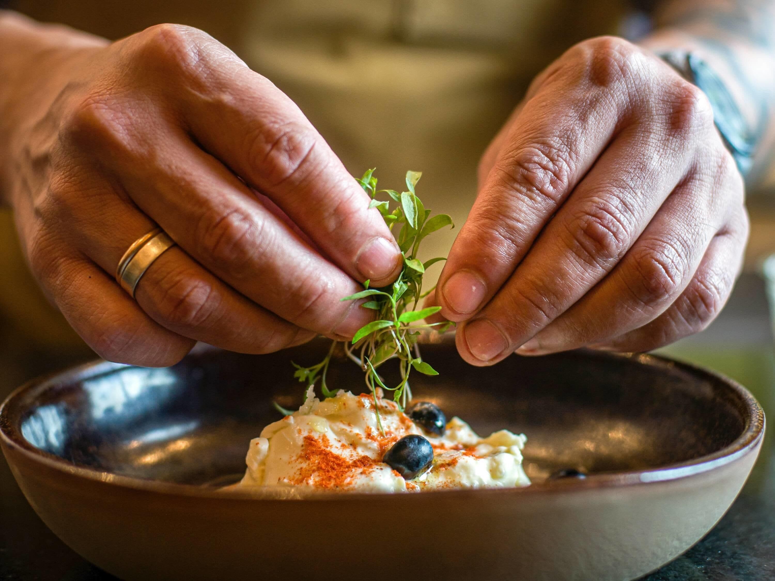 Hands placing a sprig of green herb on a bowl of food.