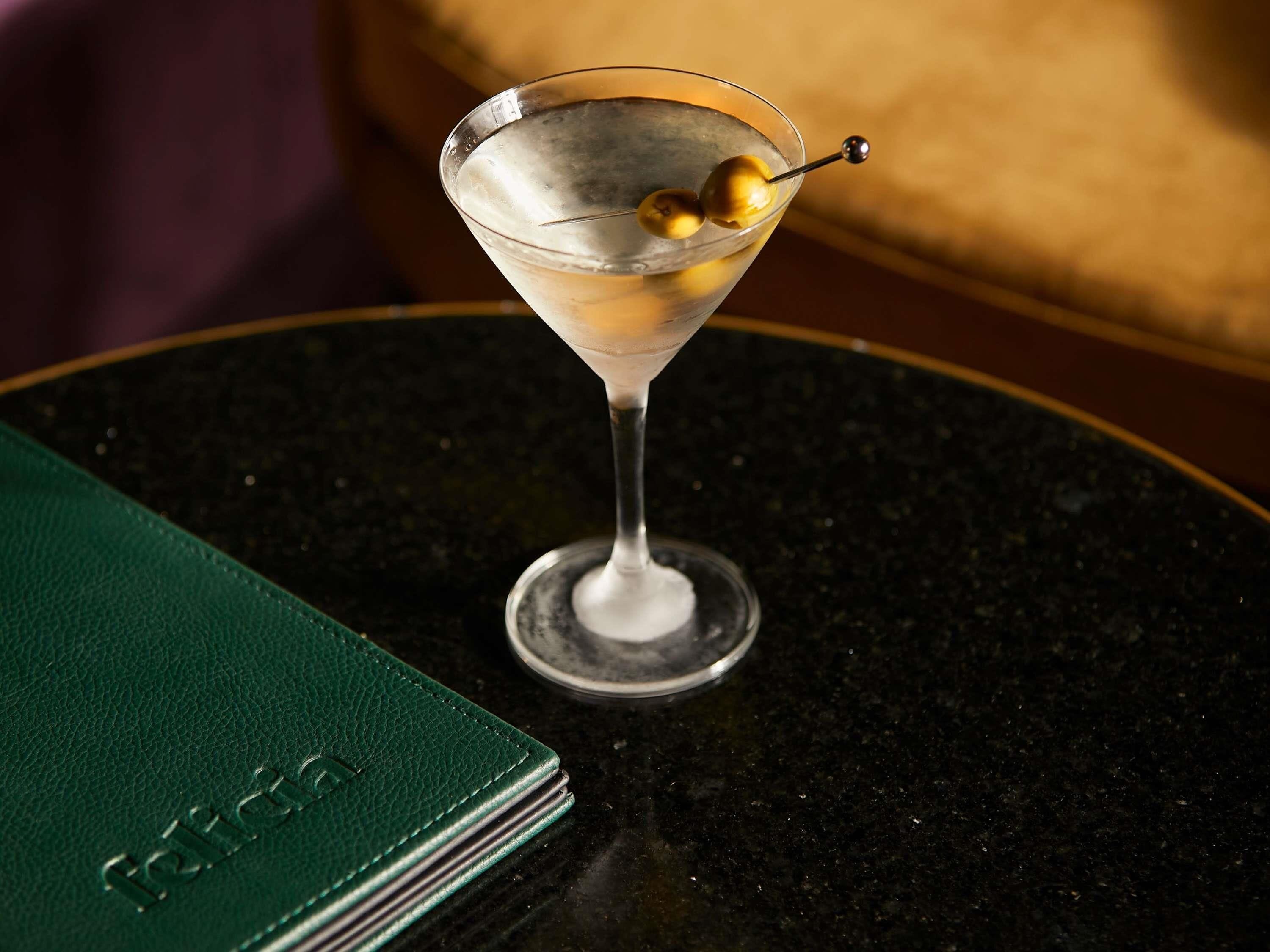 Una copa de martini con una cereza en un palillo sobre una mesa redonda.