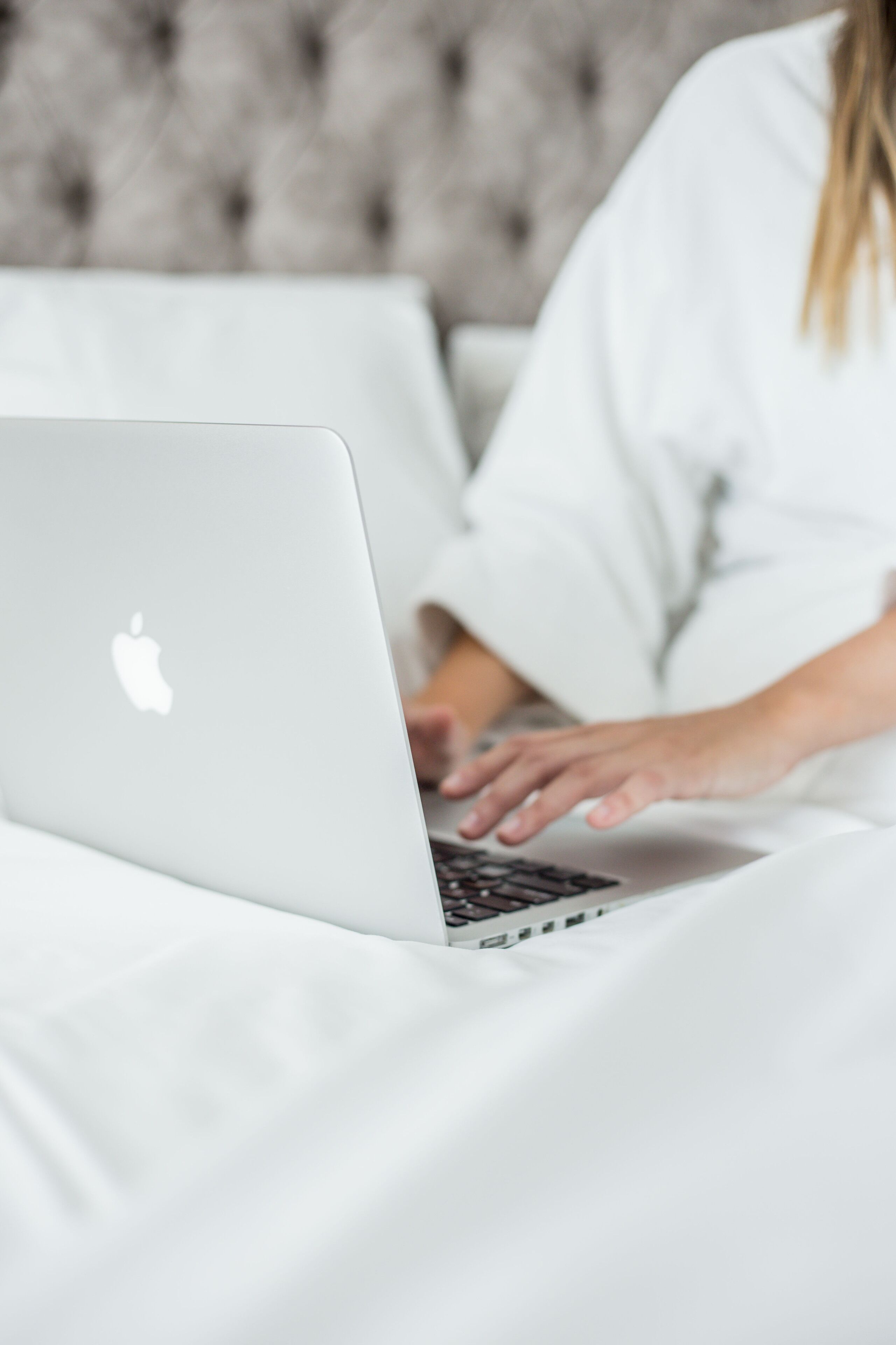 A person using a laptop on a bed with a tufted headboard.