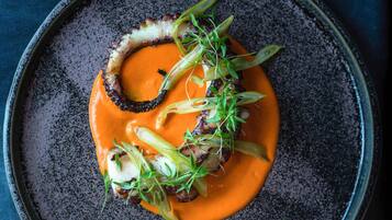 A plate of food with a sauce, greens, and a ring of what appears to be a mushroom or similar ingredient.