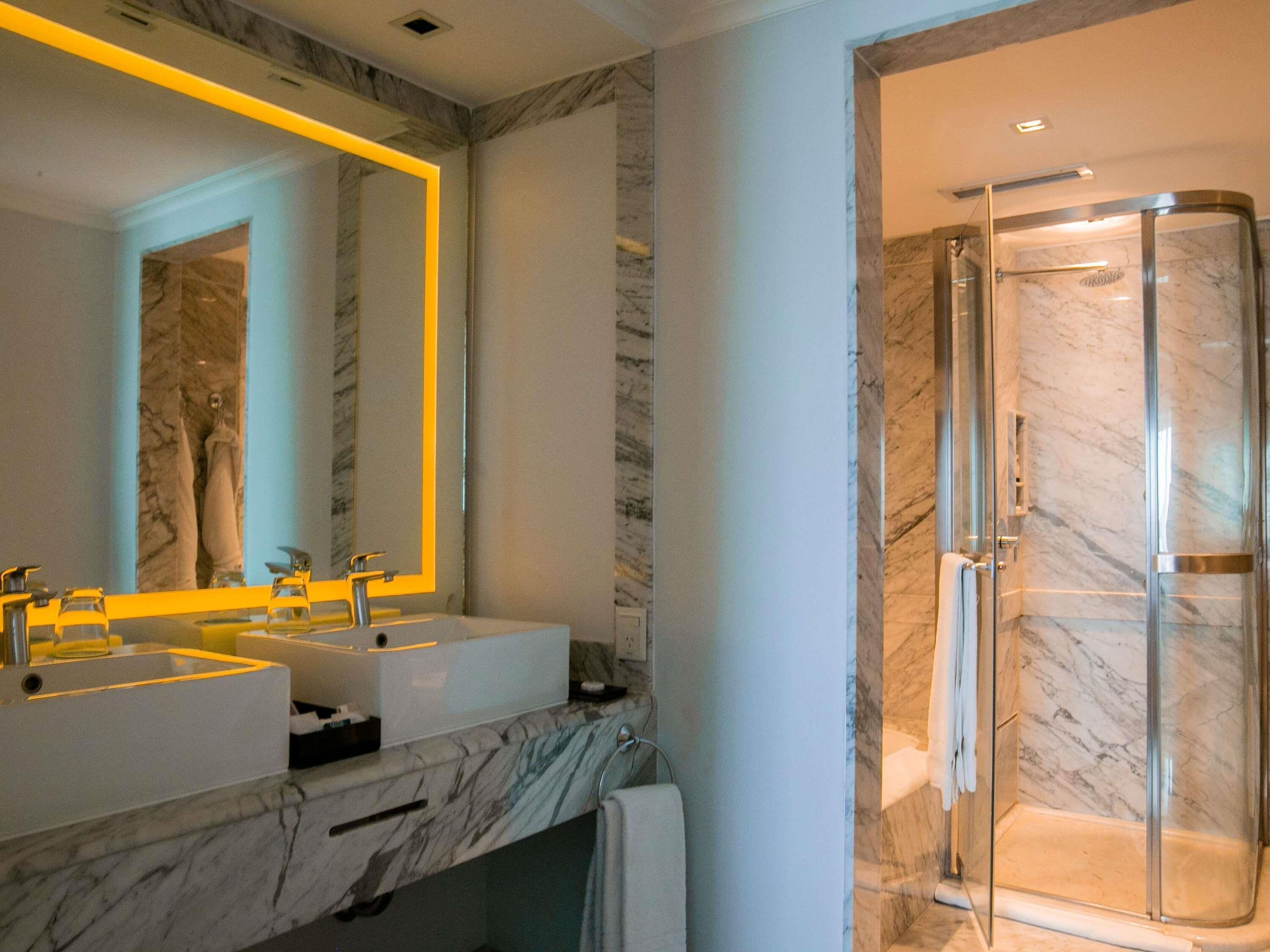 Un baño moderno con dos lavamanos, un espejo grande y una ducha con cerramiento de vidrio.