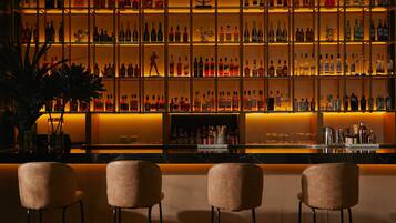 Una zona de bar con múltiples estantes llenos de botellas, una barra y tres taburetes acolchados.
