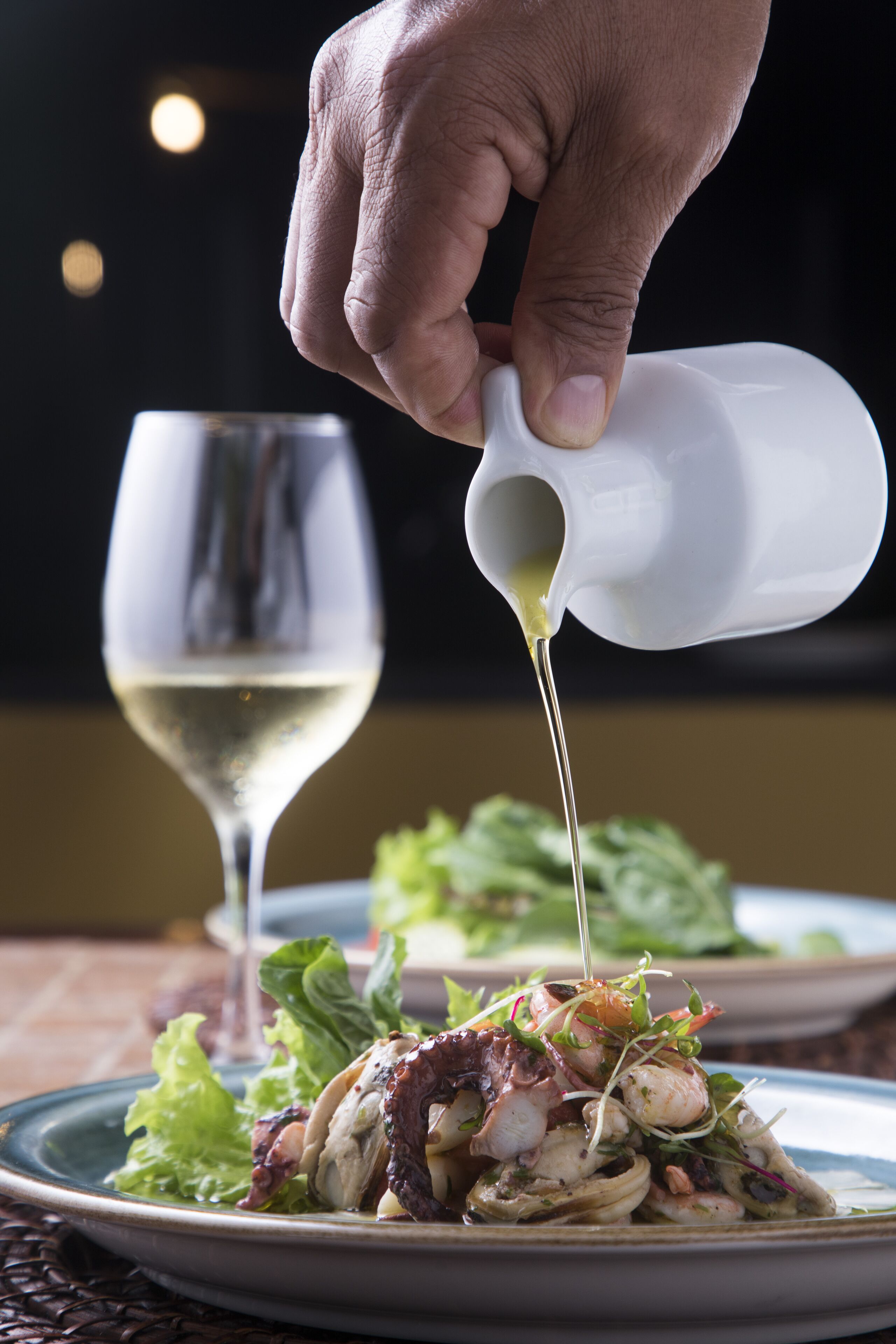 Una mano sirve un líquido transparente de una jarra blanca sobre un plato de comida.
