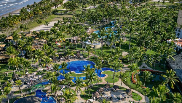 Een resort met meerdere zwembaden, palmbomen en uitzicht op de oceaan.