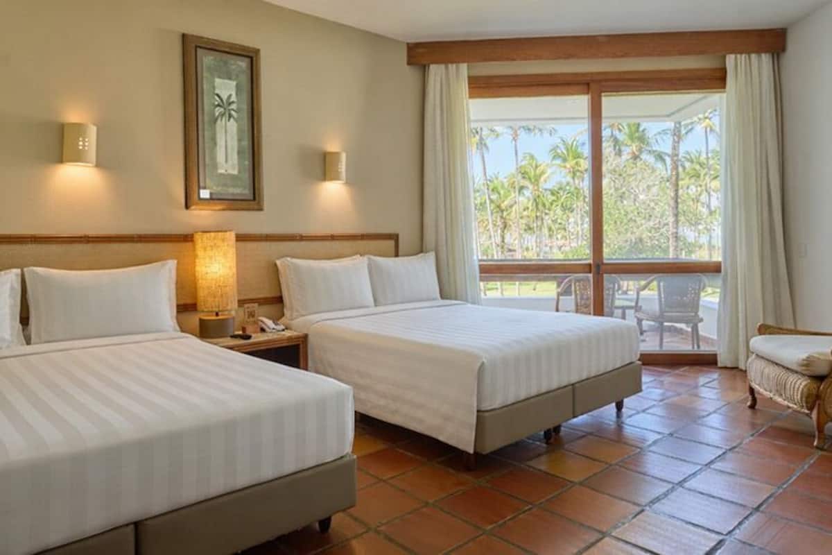 Une chambre d’hôtel avec deux lits, une chaise, une table de chevet et une grande fenêtre donnant sur des palmiers.