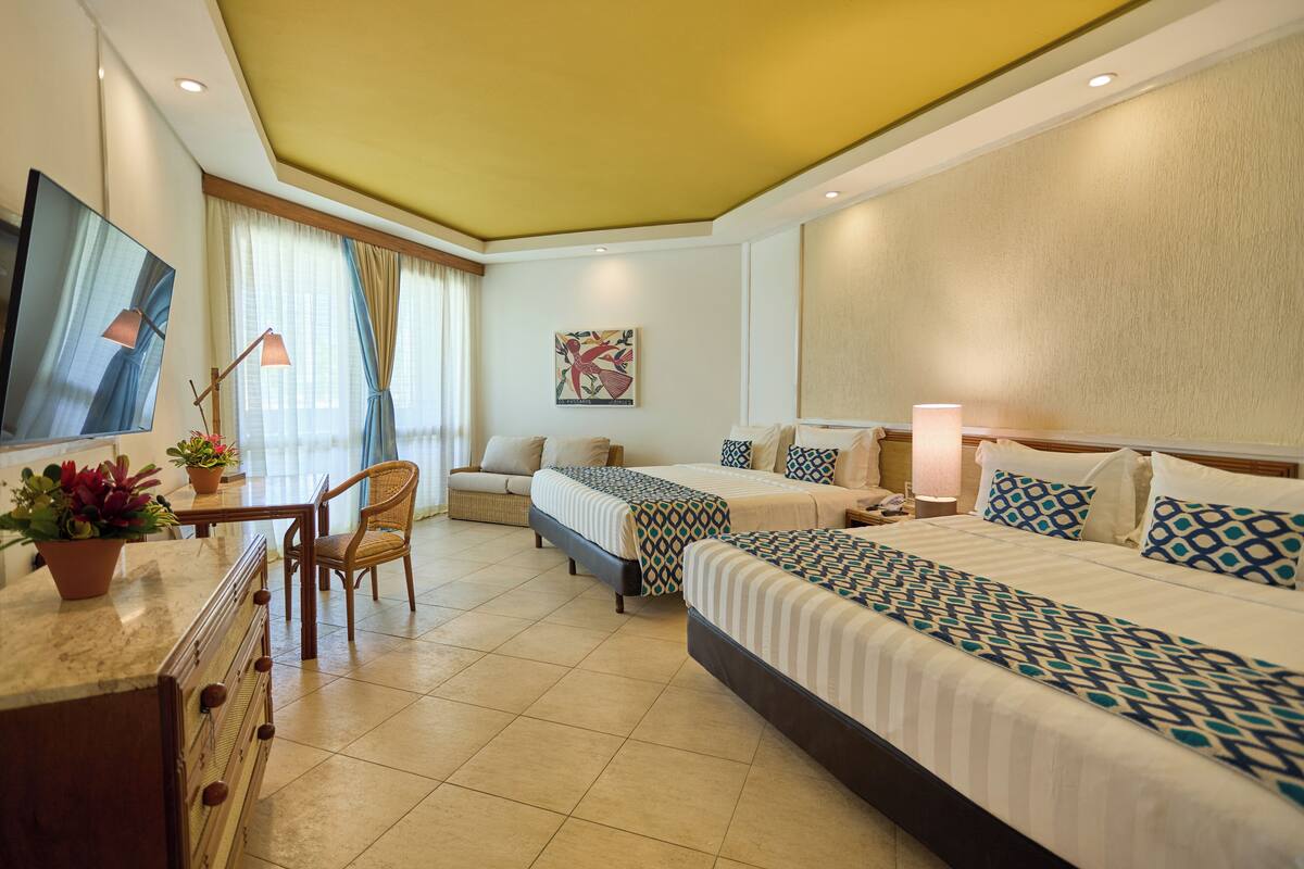 Une chambre d’hôtel avec deux lits, un bureau avec une chaise, une télévision et une fenêtre avec des rideaux.