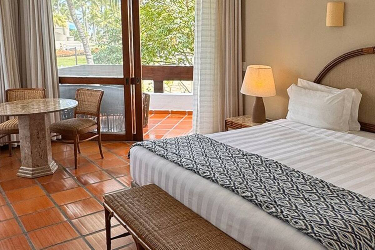 Une chambre d’hôtel avec un grand lit, une petite table ronde, deux chaises, un banc et une vue sur l’extérieur.