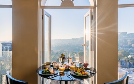A breakfast table with a variety of foods and drinks, set in a room with large windows offering a scenic view.