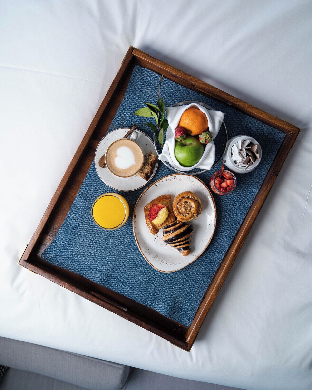 Een dienblad met een koffiekop, een bord met een gebakje, een fruitschaal en een glas sap op een bed.