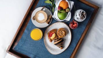 Een dienblad met een koffiekop, een bord met een gebakje, een fruitschaal en een glas sap op een bed.