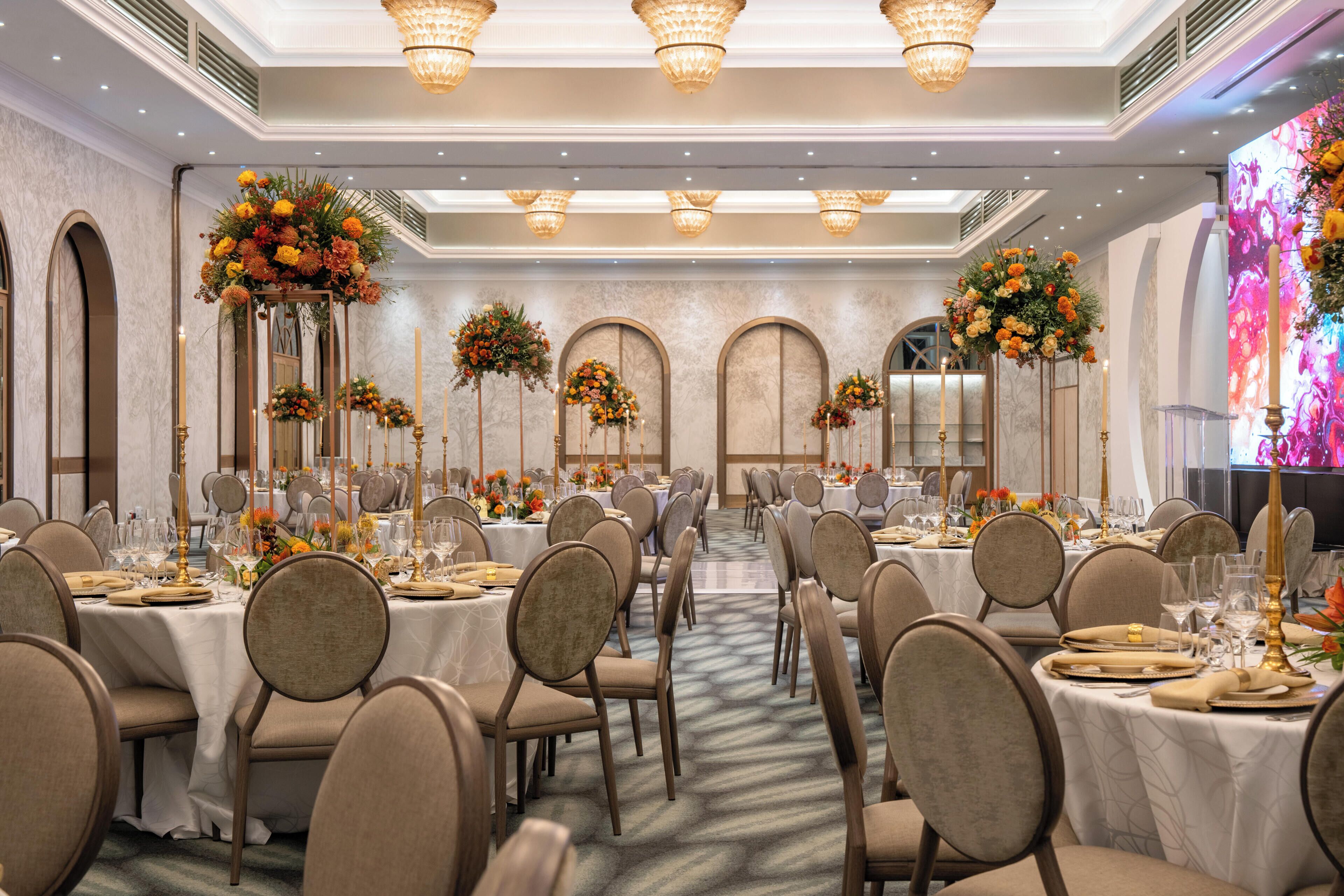 A banquet hall with round tables, chairs, and floral centerpieces.