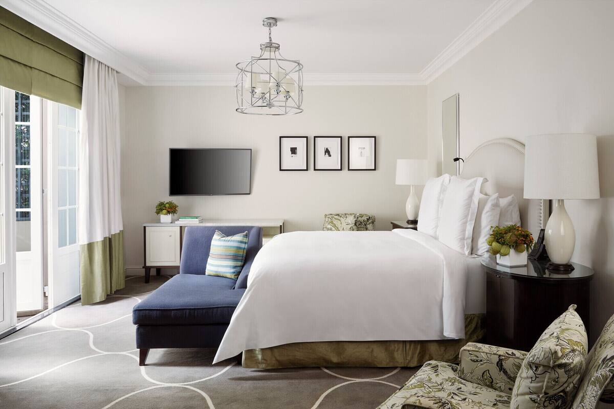 A hotel room with a bed, a desk, a chair, a TV, and a window with curtains.