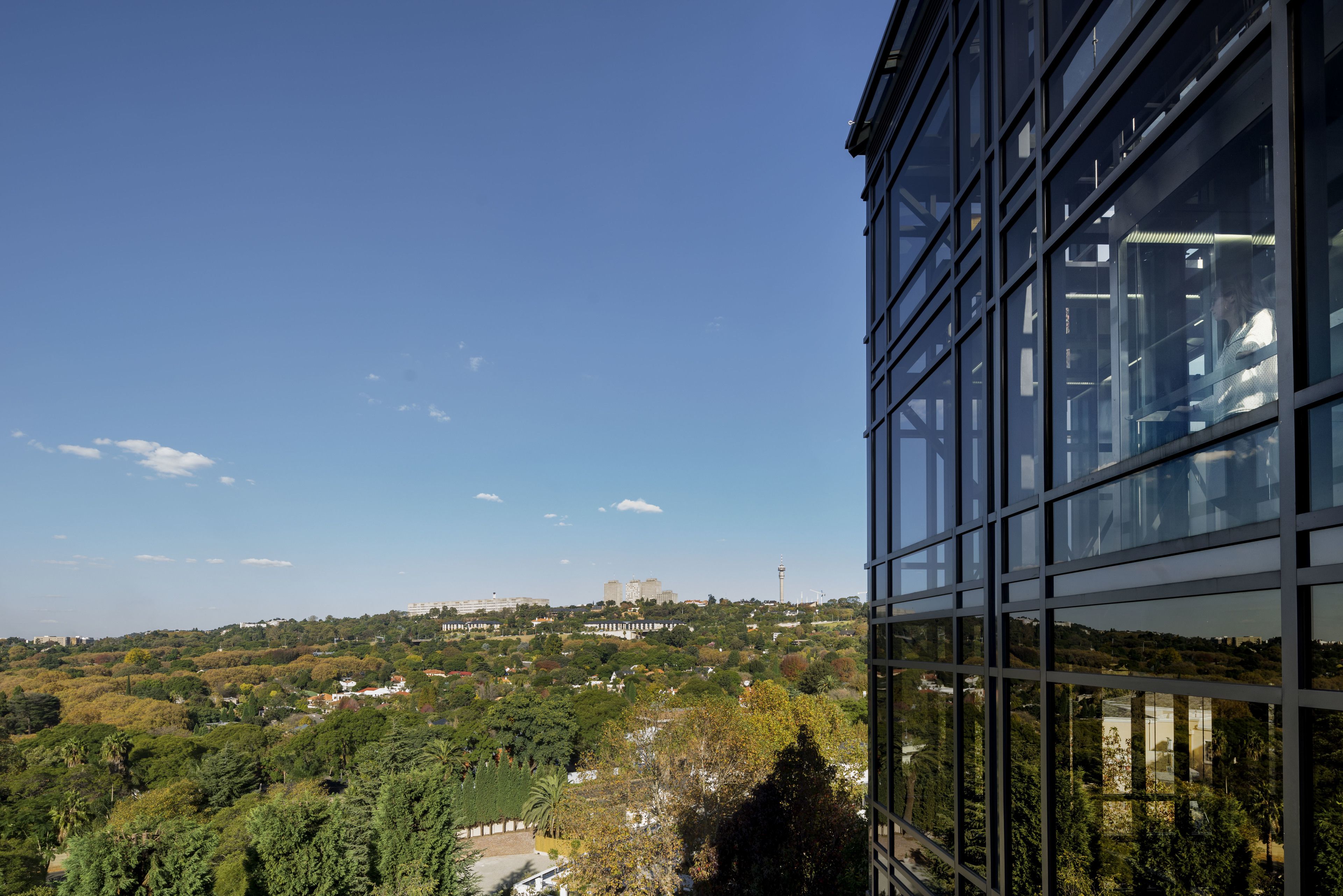 A modern building with large windows reflecting a view of a cityscape with greenery and distant buildings.