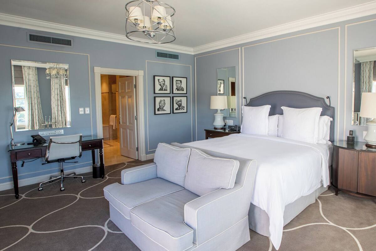 A hotel room with a large bed, a desk, a chair, a dresser, and a mirror.