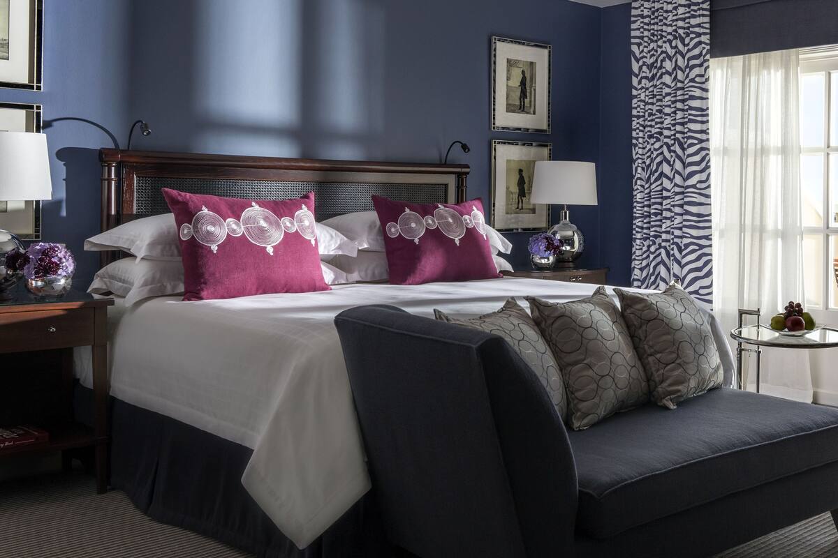 A hotel room with a large bed, a bedside table, a lamp, and a window with curtains.