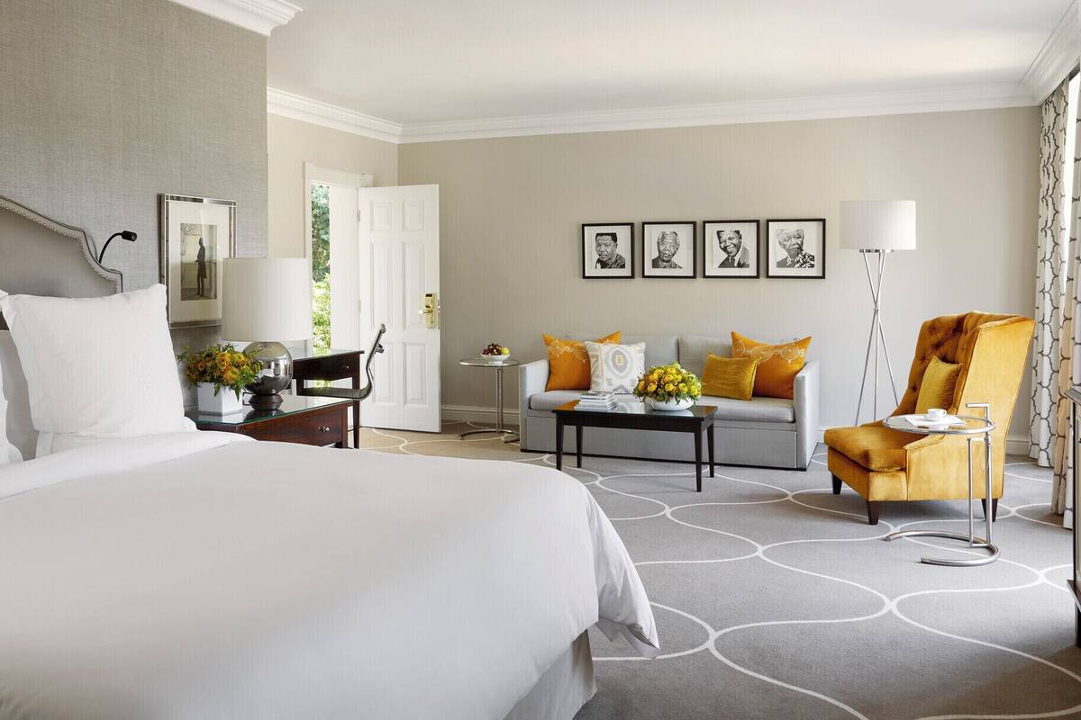 A hotel room with a bed, a sofa, a chair, a small table, and a lamp.