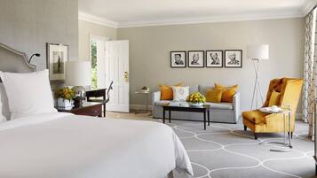 Una habitación de hotel con cama, sofá, sillón, una mesita y una lámpara.