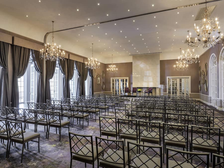 Un salón de conferencias amplio con filas de sillas, candelabros y ventanas grandes.