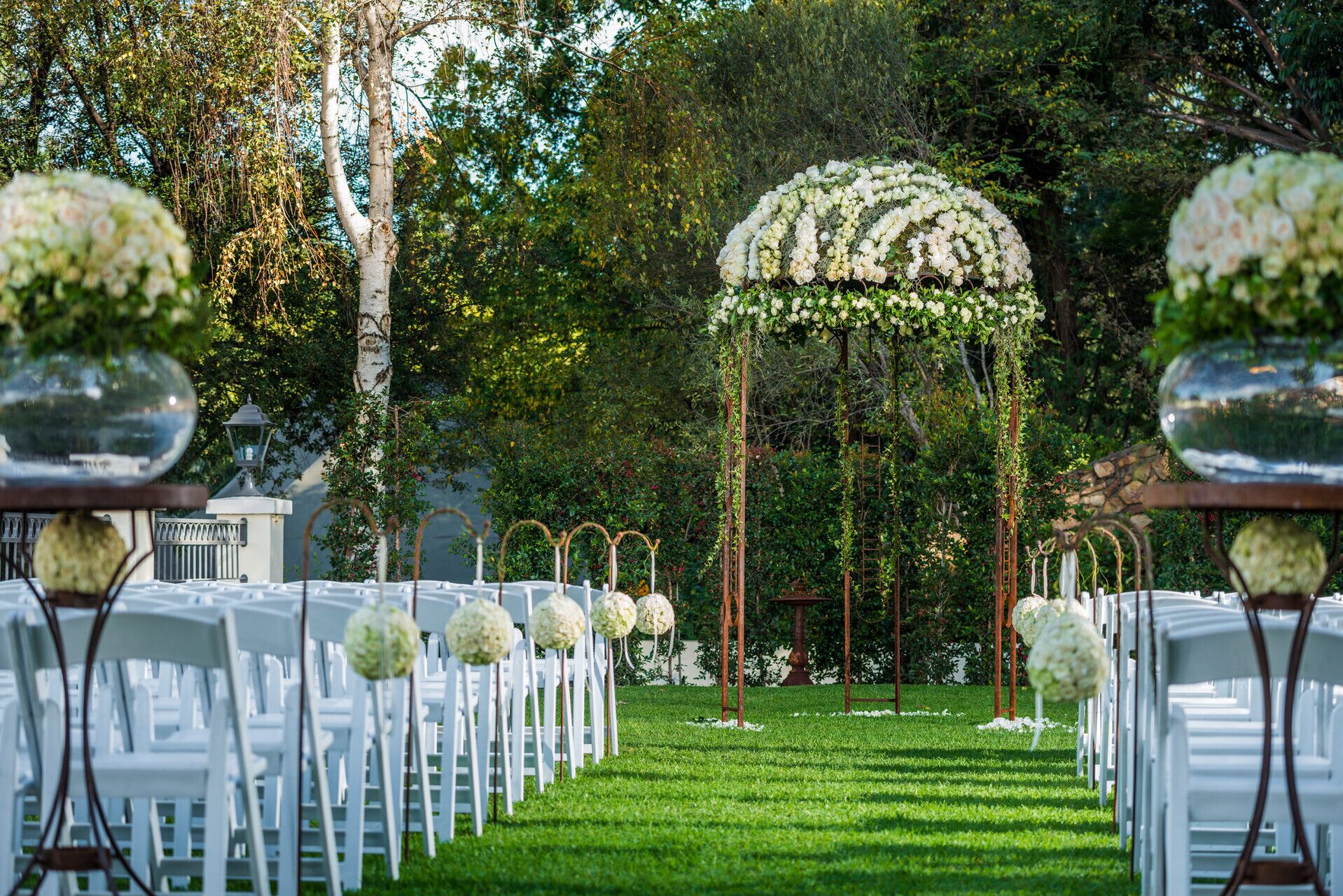 Un pasillo nupcial con sillas blancas y decoración floral.