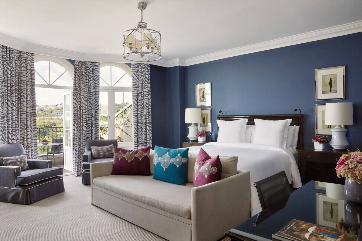 A hotel room with a large bed, a sofa, a desk, and a balcony with curtains.