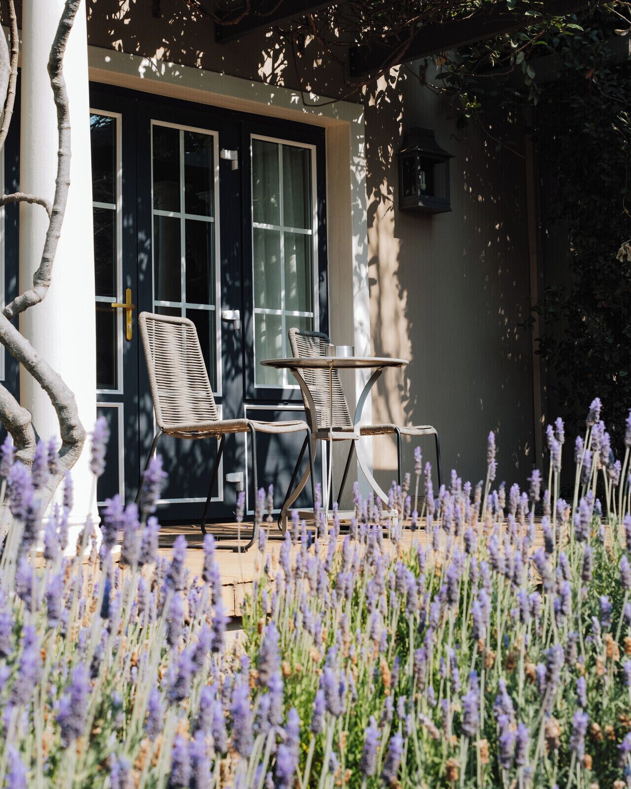 A patio with wicker chairs and a table, a door with glass panels, and a garden with lavender.