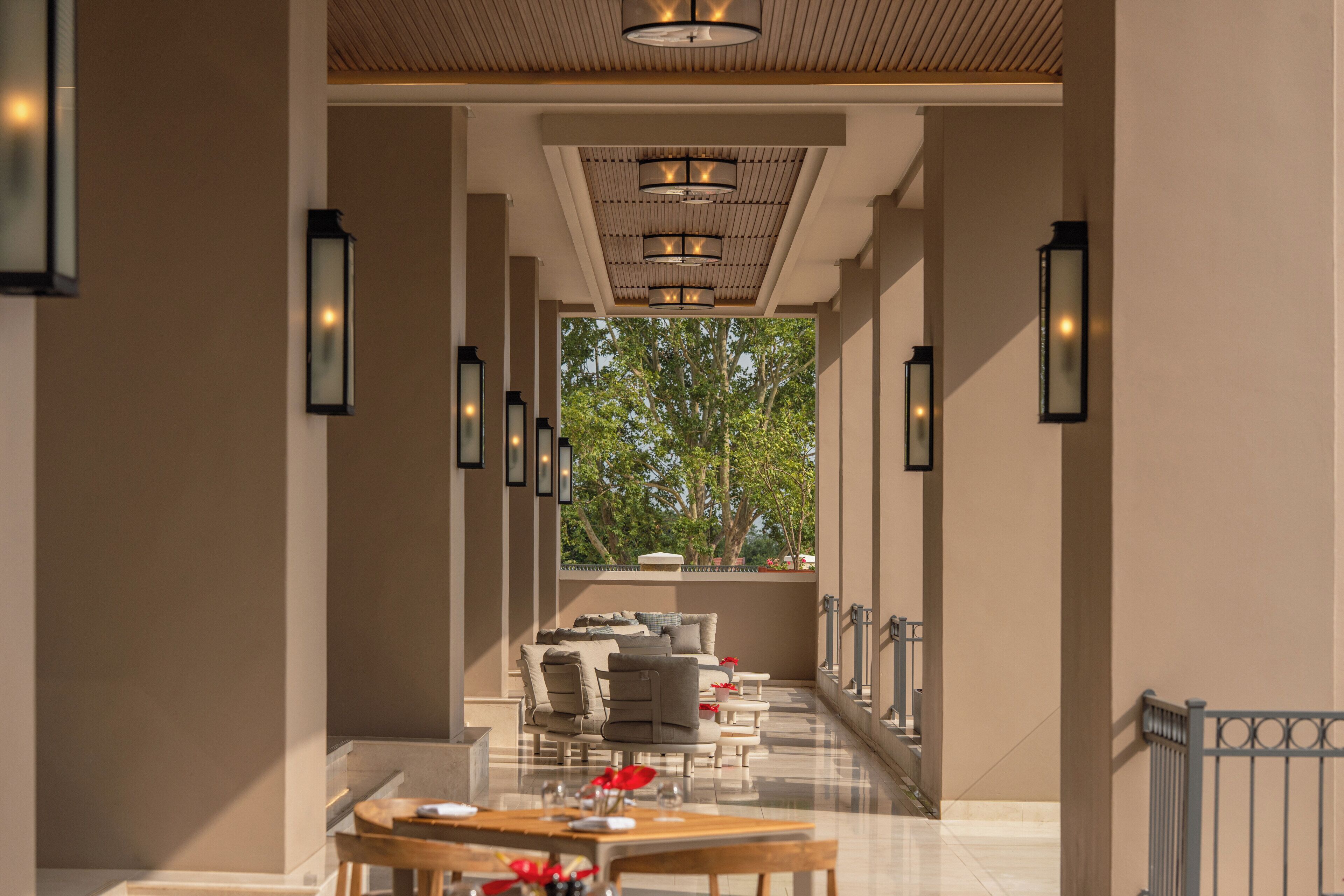 Un pasillo que conduce a un comedor con vistas a árboles, techo de madera e iluminación en las paredes.