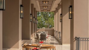 A corridor leading to a dining area with a view of trees, a wooden ceiling, and wall-mounted lights.