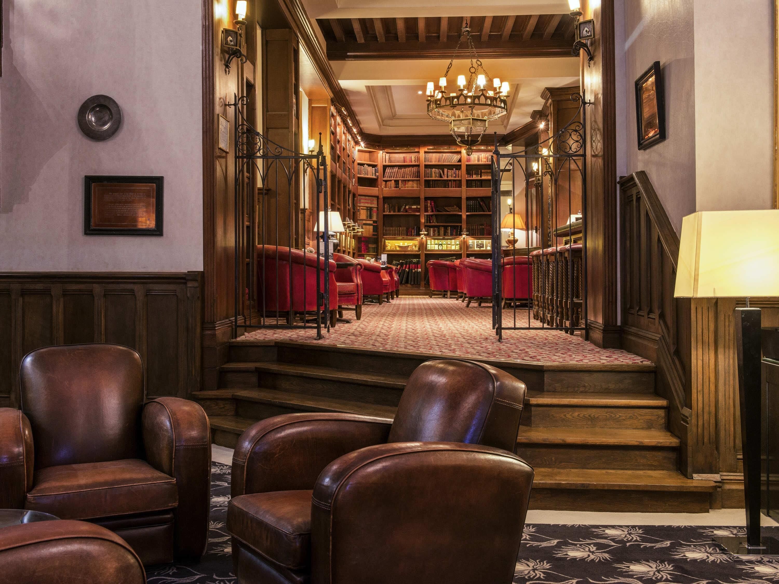 A library with leather chairs, bookshelves, and a chandelier.