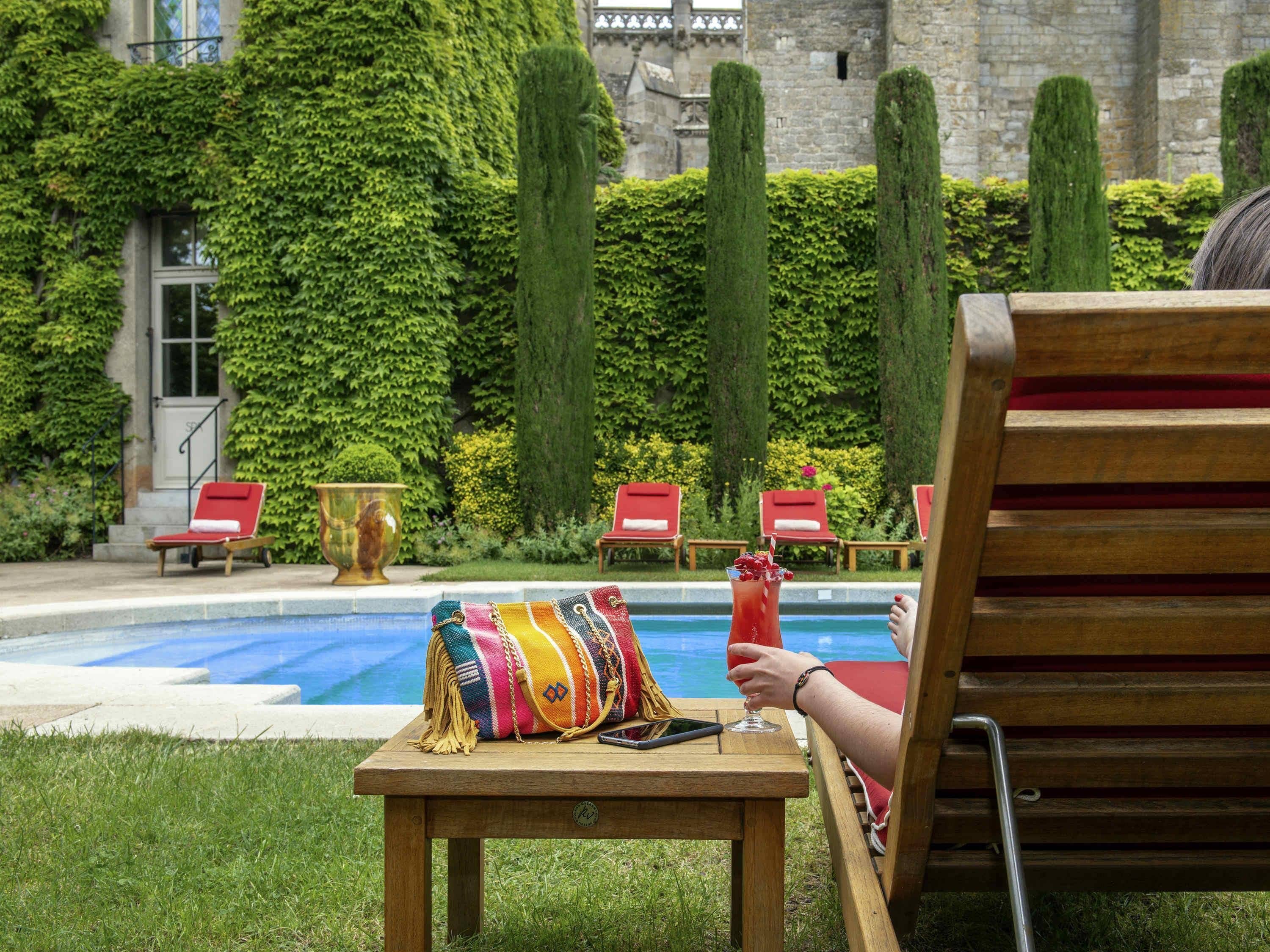 A poolside area with a lounge chair, a colorful bag, and a drink.