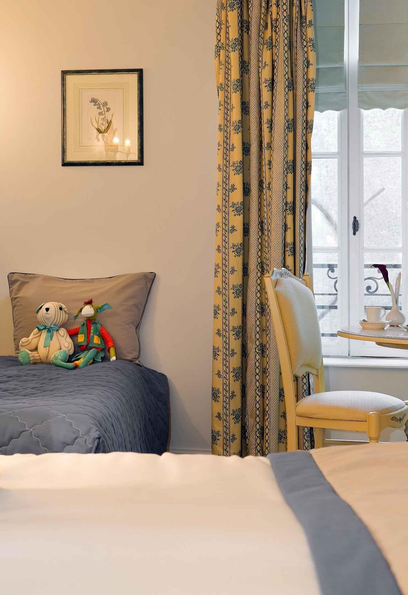 Un dormitorio con una cama, una silla, una mesita y un cuadro en la pared, además de cortinas.