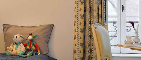 Un dormitorio con una cama, una silla, una mesita y un cuadro en la pared, además de cortinas.
