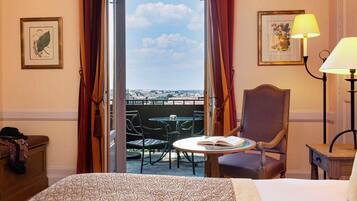 A hotel room with a bed, a chair, a table with a book, a lamp, and a balcony with a view.