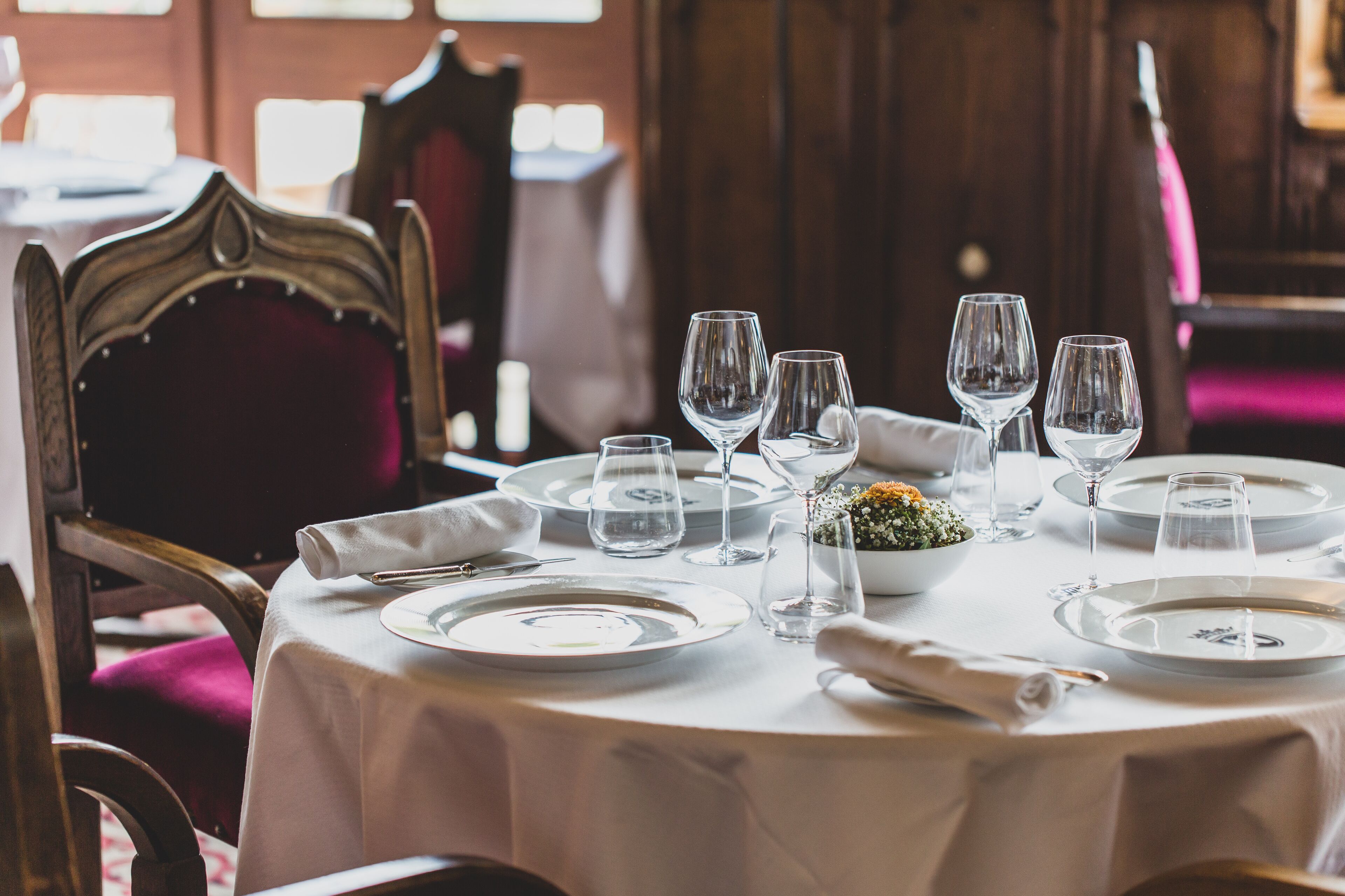 Une table à manger dressée avec des assiettes, des verres et un petit vase rempli de fleurs.