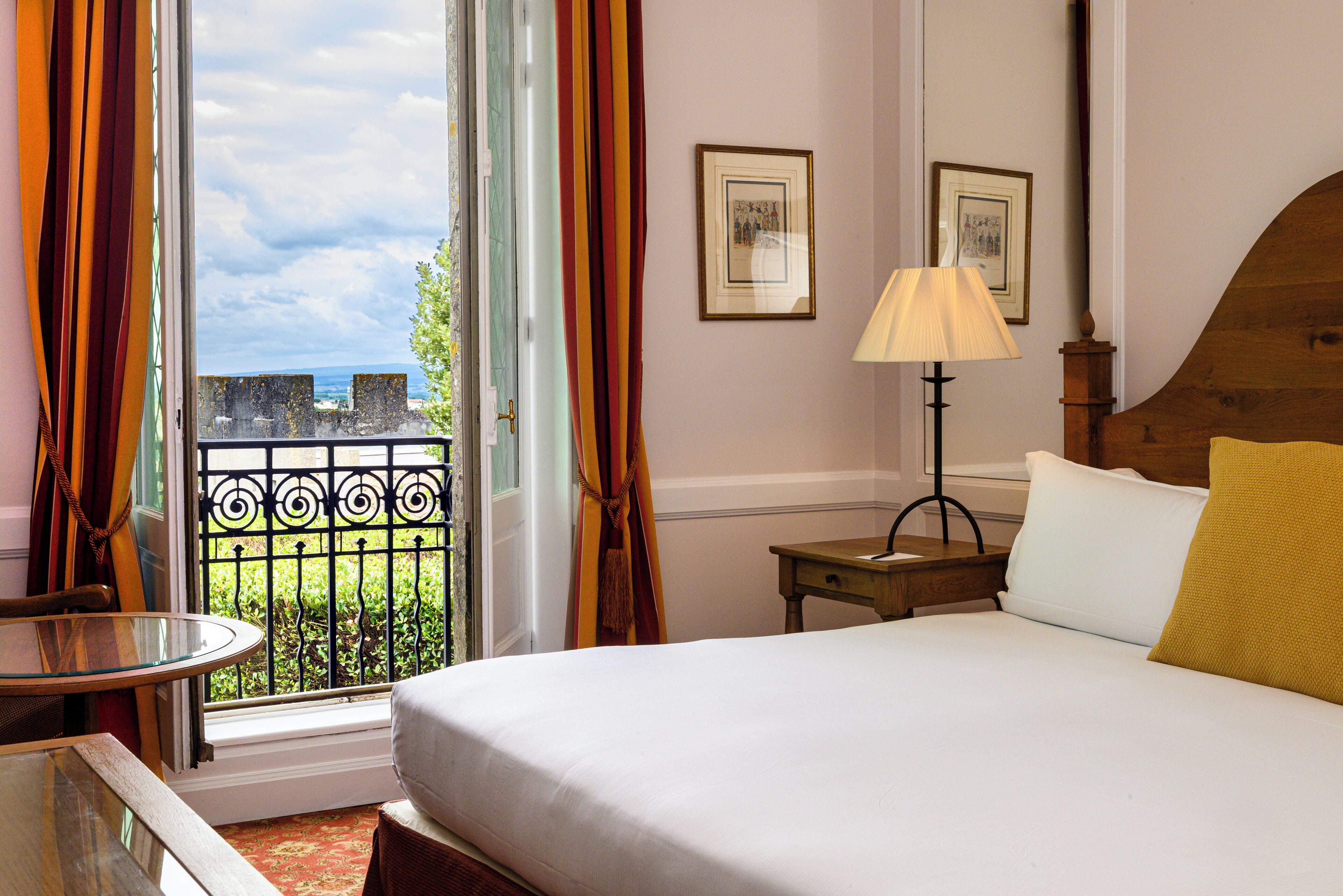 A hotel room with a bed, a table, a lamp, and a view of the outside.