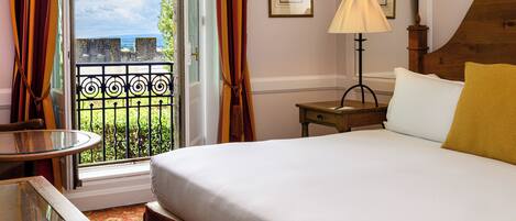 A hotel room with a bed, a table, a lamp, and a view of the outside.