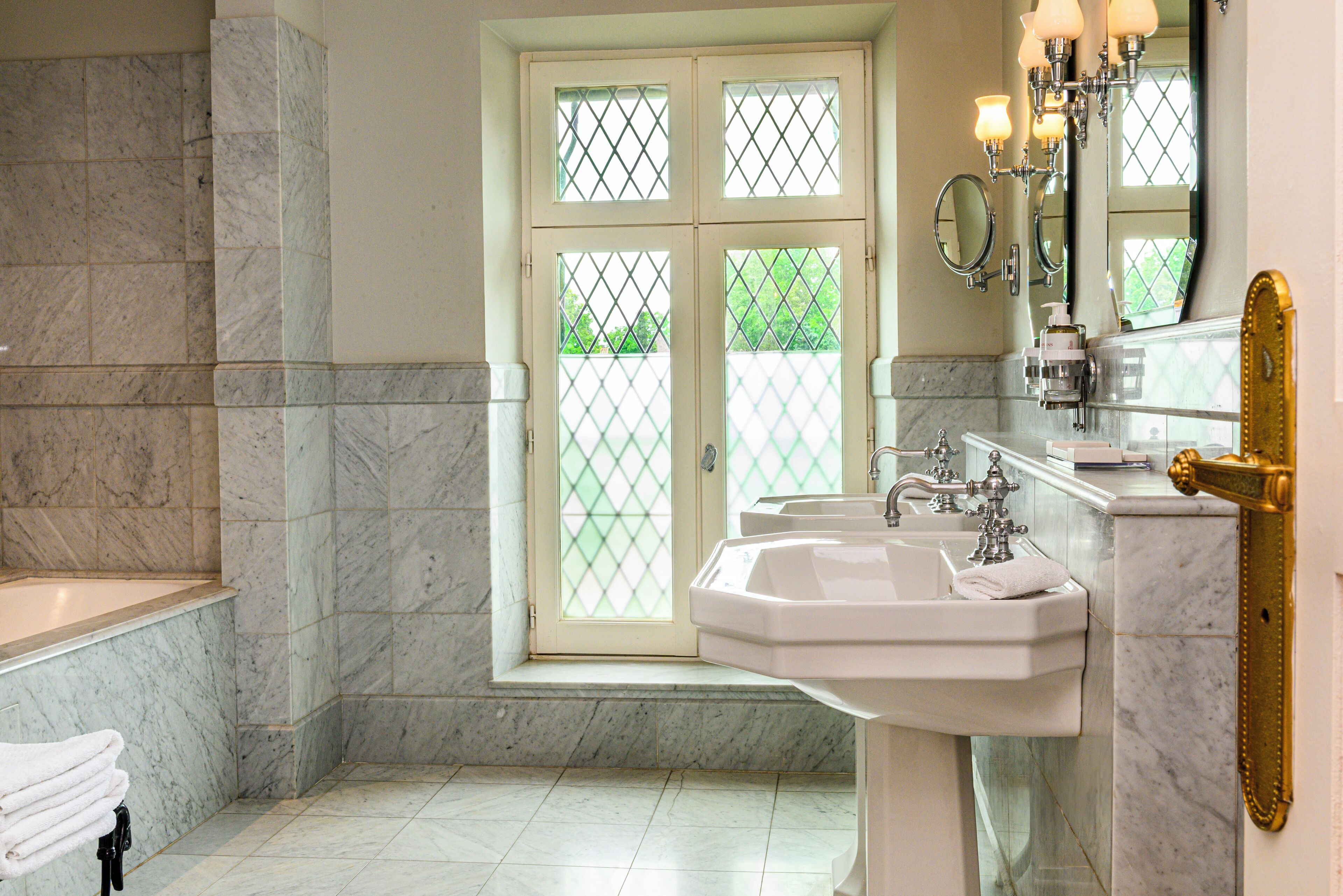 A bathroom with a marble floor, a sink, and a window with a view of greenery.
