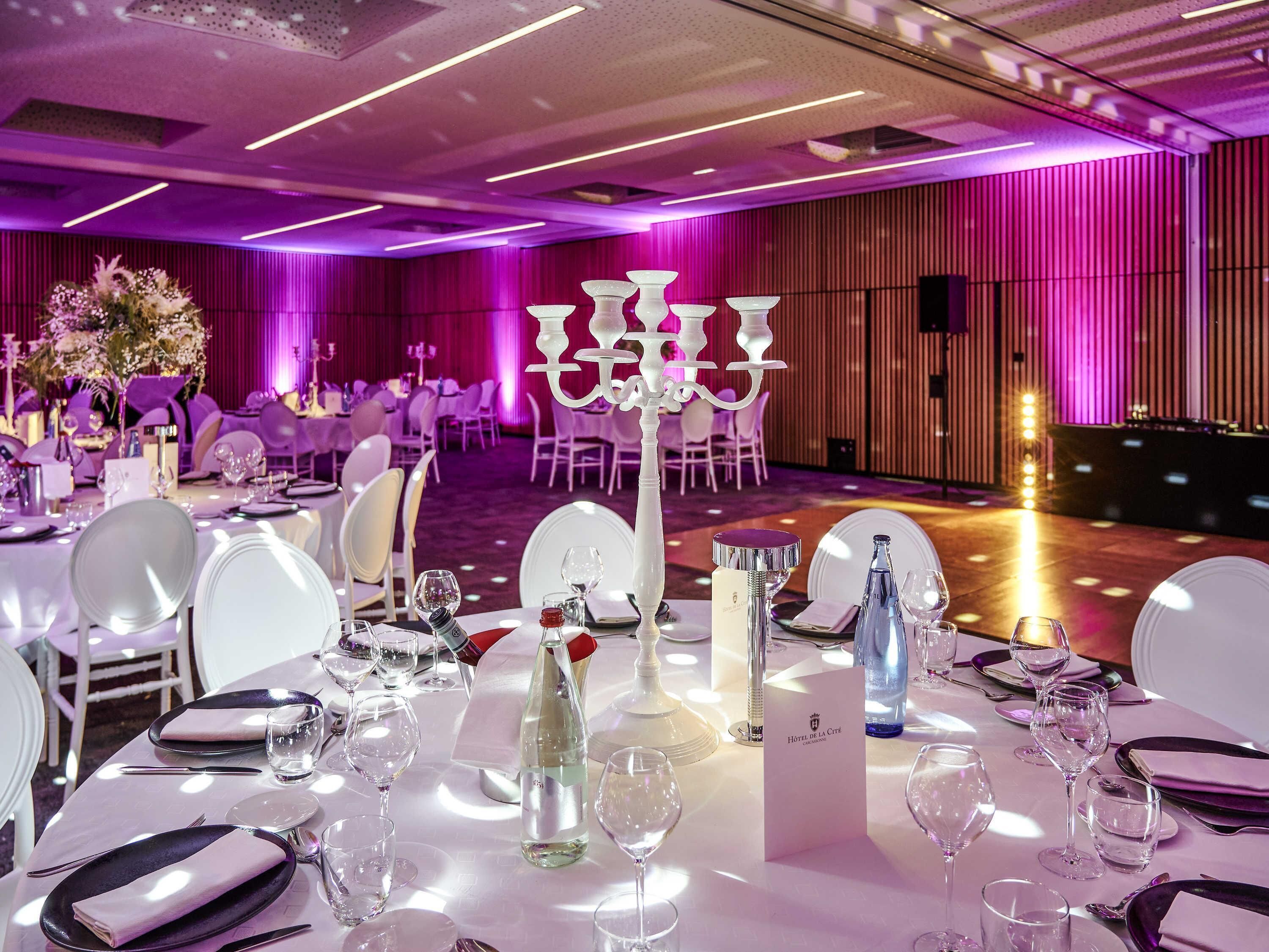 A banquet hall with tables set for a formal event, featuring white tablecloths, plates, and glasses.