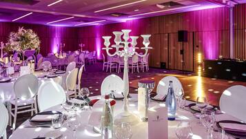 Un salón de banquetes con mesas dispuestas para un evento formal, destacando manteles blancos, platos y copas.