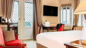 Habitación de hotel con una cama grande, un escritorio con una silla, un televisor y cortinas estampadas.