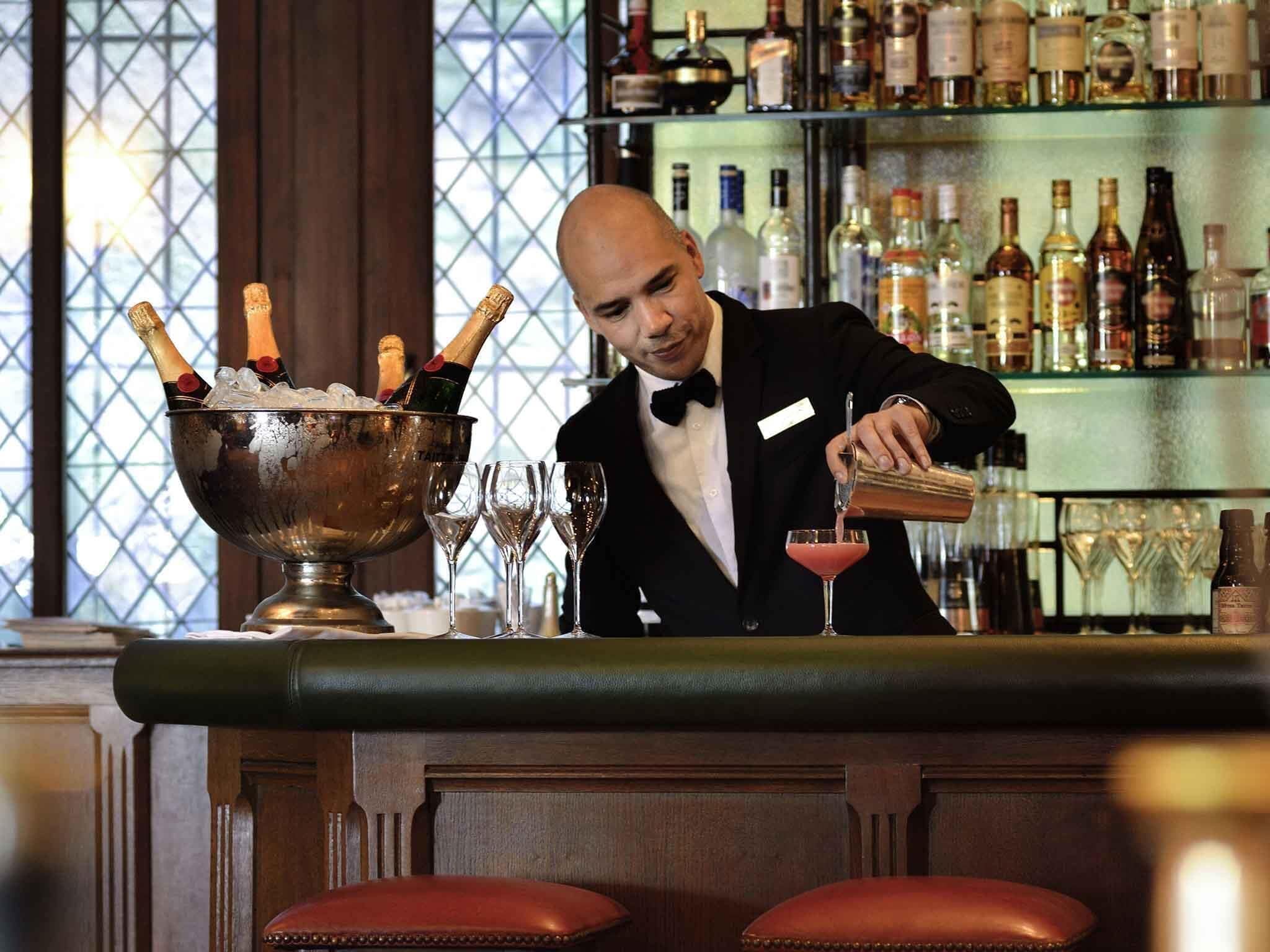 A bar setting with a bartender pouring a drink into a glass, a bowl of ice with champagne bottles, and a bar stocked with various bottles.