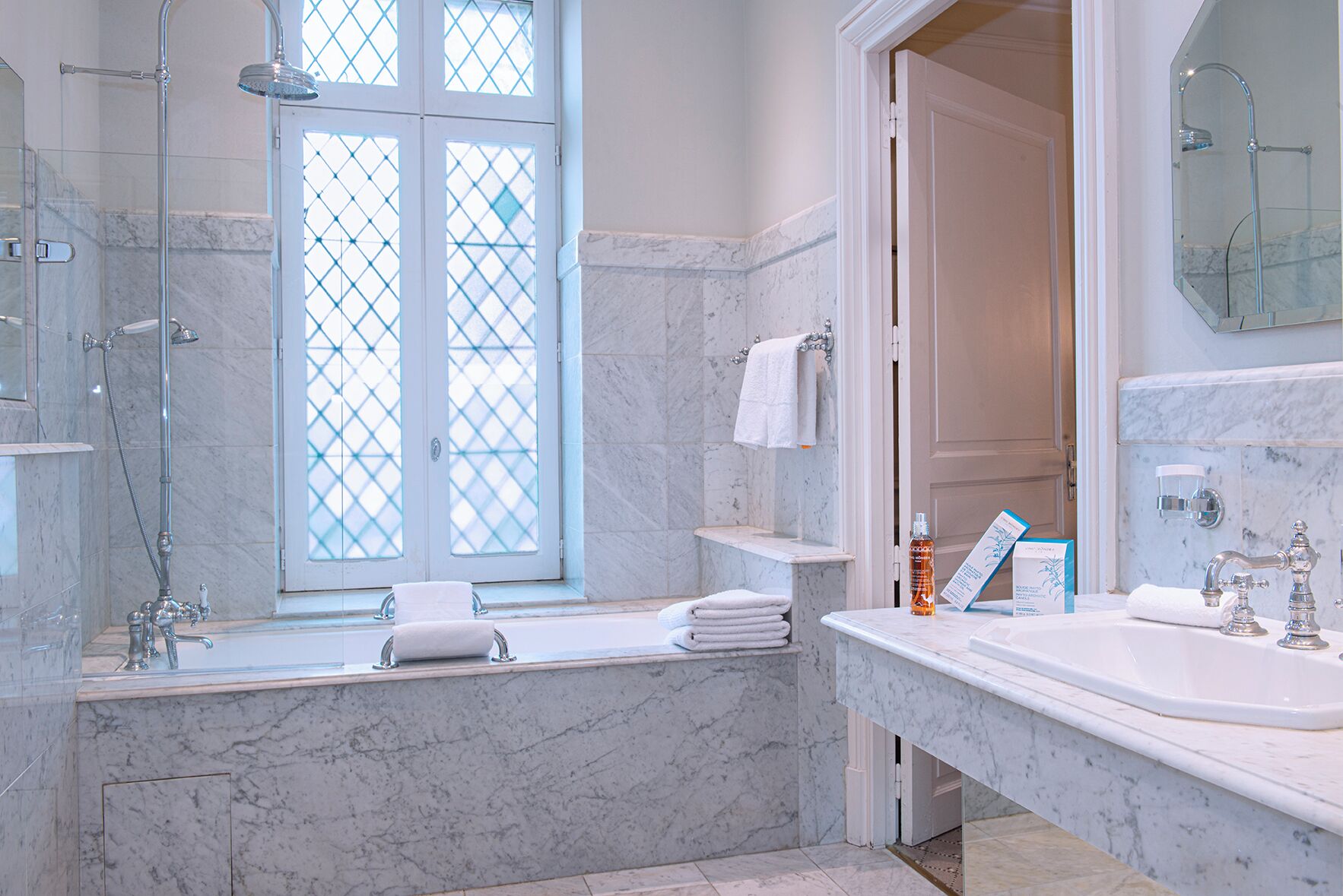 A modern bathroom with a glass-enclosed shower, a marble bathtub, and a large mirror above the sink.