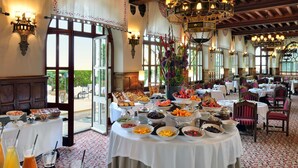 Un comedor con mesas dispuestas para el desayuno, una araña de cristal y vistas a través de la puerta abierta.