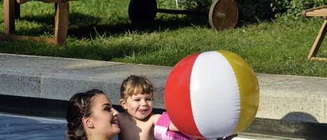 Une piscine avec un ballon de plage rouge et blanc, une chaise longue et une serviette.