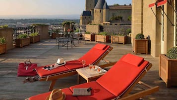 A rooftop terrace with lounge chairs, a table with drinks, and a view of a castle.