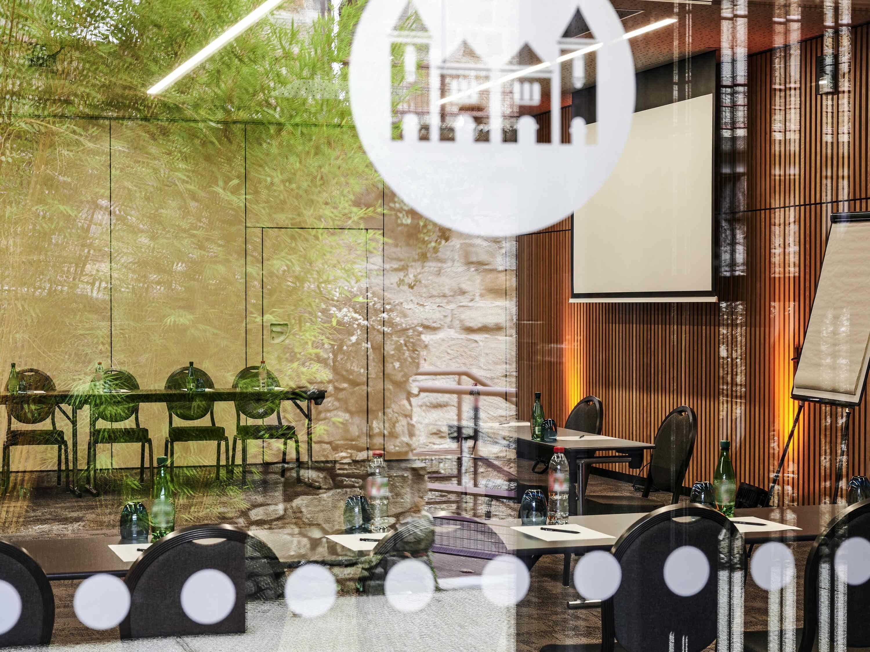 Une salle de conférence dotée d’une table en verre, de chaises, d’un écran de projection et d’un mur en pierre.