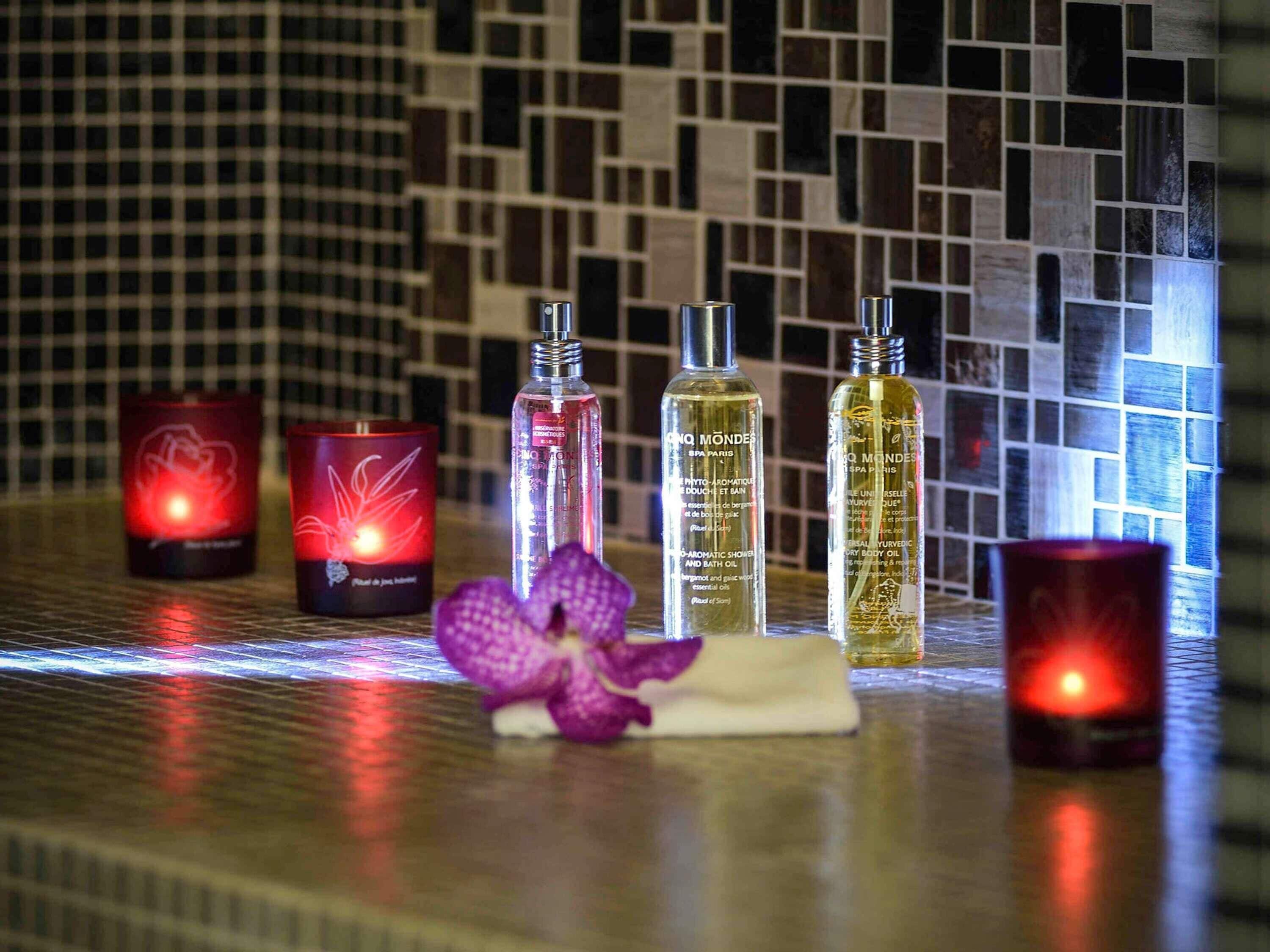 Candles, bottles of oil, and a purple orchid on a tiled surface.
