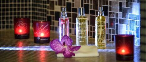 Candles, bottles of oil, and a purple orchid on a tiled surface.