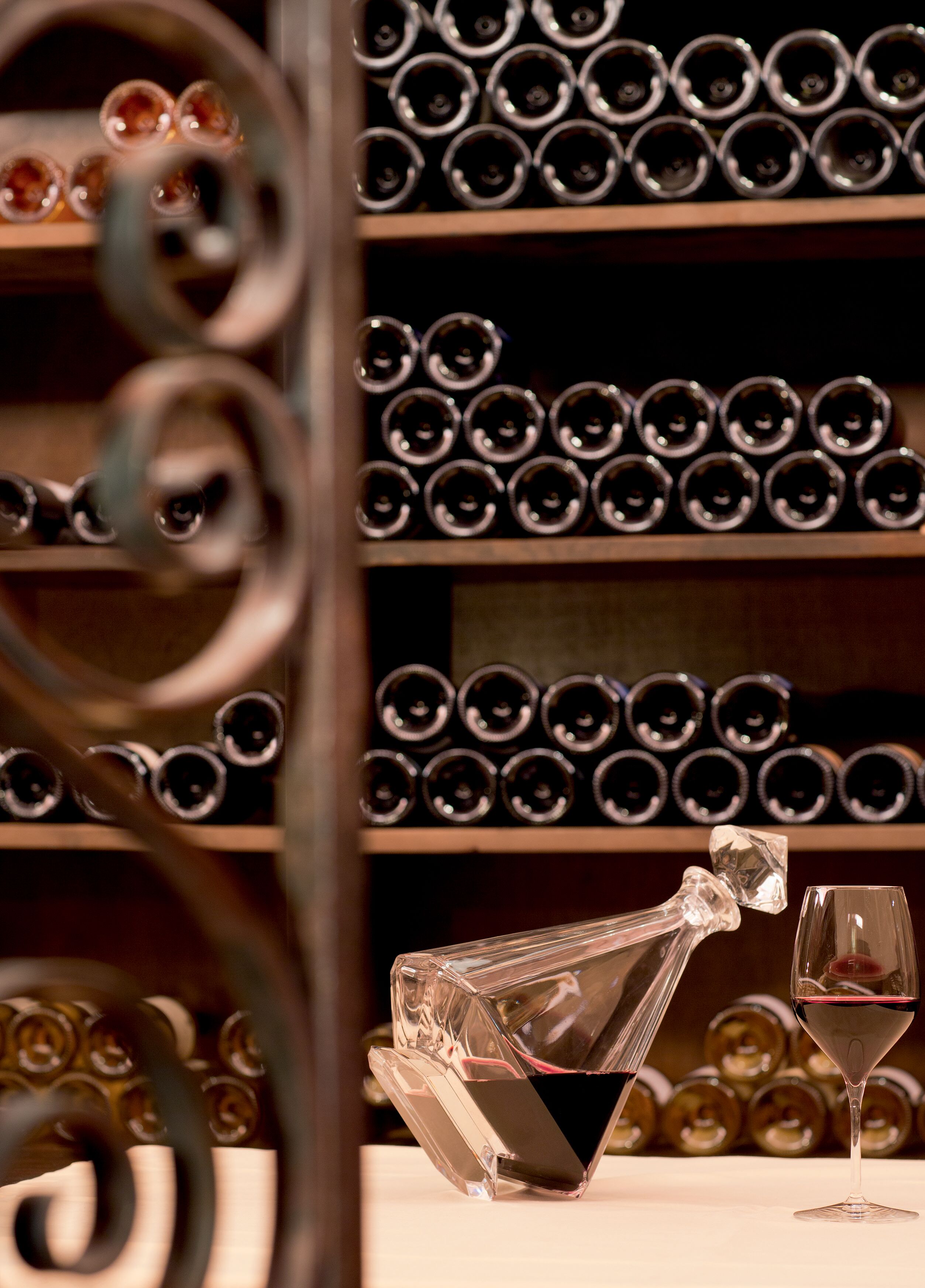 A wine bottle and glass on a table with a background of neatly arranged wine bottles on shelves.