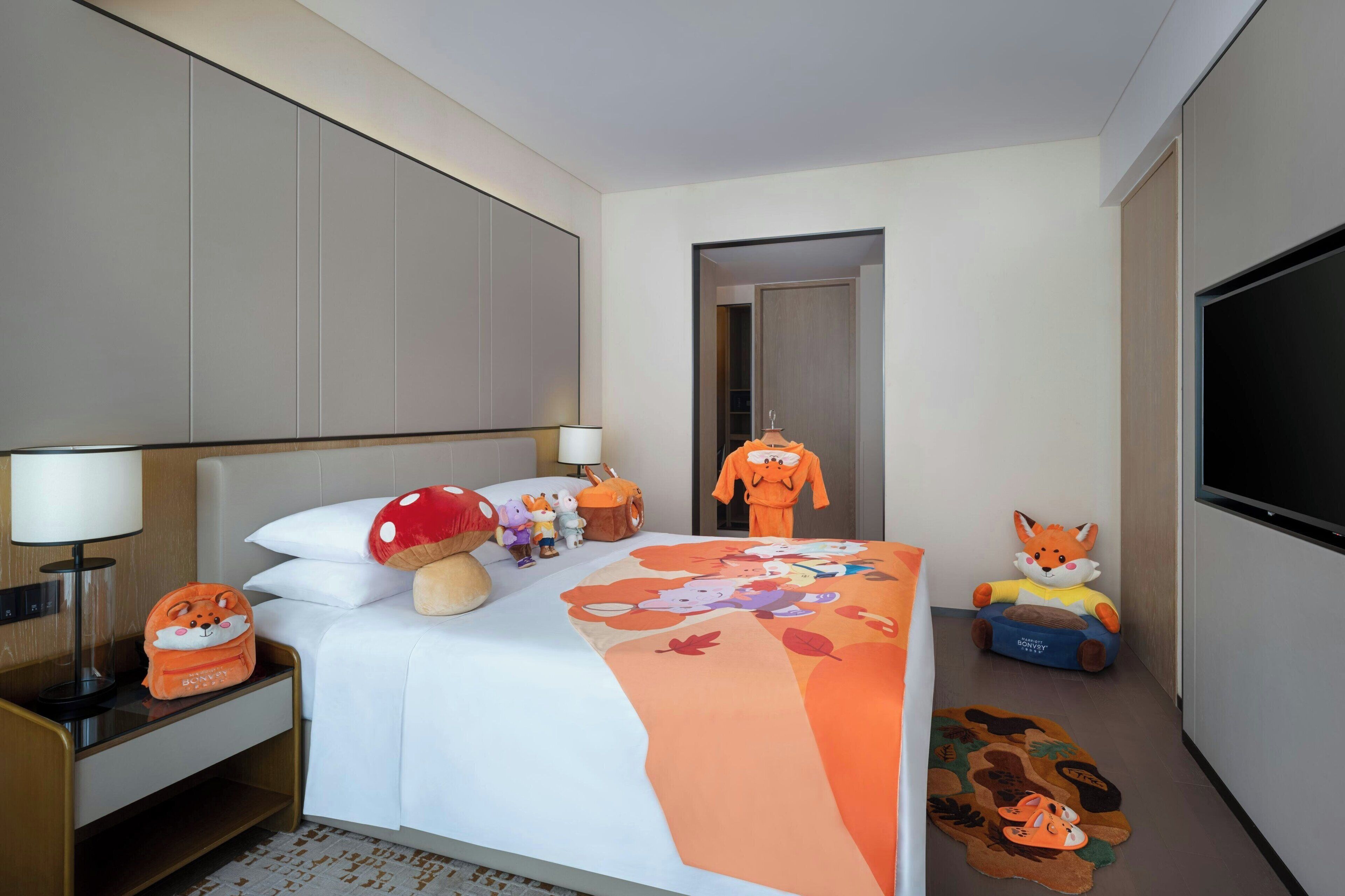 Een hotelkamer met een bed, kussens, een lamp, een televisie en pluche knuffels.