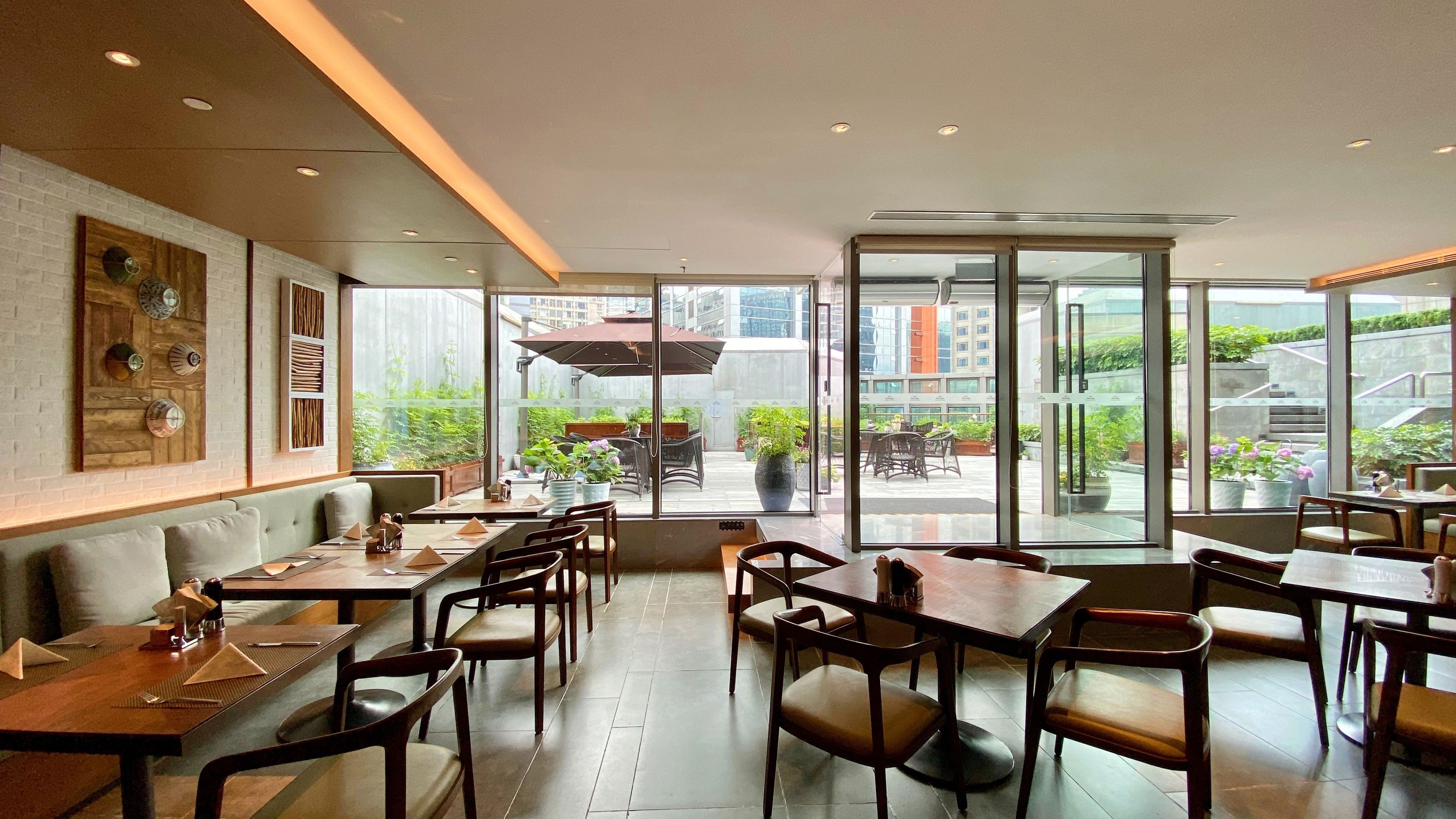 Un restaurante moderno con terraza, que cuenta con mesas y sillas de madera, y una pared de ladrillo con platos decorativos.